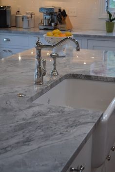 a white kitchen with marble counter tops and stainless steel faucet, in the middle of an island