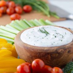 a wooden bowl filled with ranch dressing surrounded by vegetables