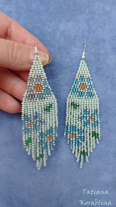 a pair of beaded earrings is being held by someone's hand on a blue background