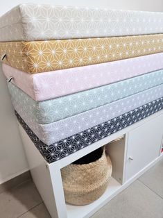 a stack of folded sheets sitting on top of a white shelf next to a basket