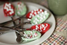 spoons with green and red candy on them sitting on a white plate next to a cup