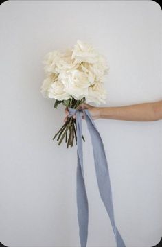 a bouquet of white flowers being held by someone's hand with ribbon around it