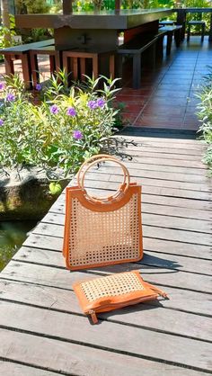 an orange purse sitting on top of a wooden platform next to a small pond with purple flowers