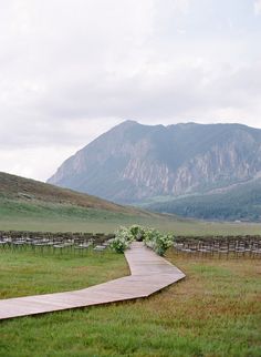 a wooden walkway in the middle of a grassy field with mountains in the background at an outdoor wedding venue