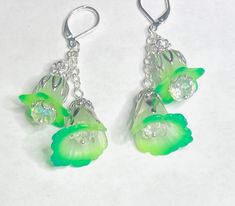 a bold and extraordinary fusion of fluorescent green hues and whimsical fairy vibes. These earrings radiate with vibrant, eye-catching colors, showcasing hand-painted petals that seem to dance with electric energy. Inspired by the captivating glow of fairies, they evoke a sense of wonder and enchantment, making a statement that is both daring and magical. At the heart of these earrings are delicate white flowers, adorned with hand-painted petals in captivating shades of florescent and phthelo green. Each petal is a work of art, showcasing intricate details and a mesmerizing color palette that will catch the eye of everyone around you. Inside each flower, a sparkling clear crystal resides, adding a touch of brilliance and enhancing the overall glamour of the design. The crystals catch the l Whimsical Green Dangle Jewelry, Green Dangle Flower Earrings For Spring, Whimsical Flower Earrings For Spring, Green Flower Earrings For Spring, Whimsical Green Nickel-free Jewelry, Whimsical Green Dangle Earrings, Green Spring Jewelry With Ear Wire, Handmade Green Dangle Flower Earrings, Bohemian Green Flower Charm Earrings