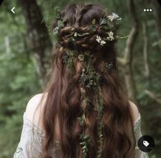 a woman with long brown hair and flowers in her hair is standing in the woods