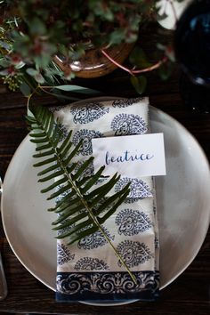 a place setting with blue and white napkins, silverware, and greenery