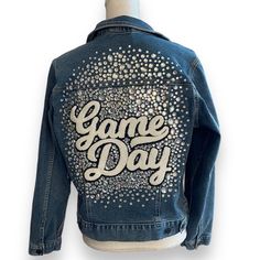 Get ready to stand out on game day with our custom upcycled denim jacket! Each jacket is meticulously handcrafted to order, ensuring a unique piece that reflects your personal style. Featuring the words 'GAME DAY' proudly emblazoned on the back with a plush chenille patch, this jacket adds a touch of vintage-inspired charm to your ensemble. But that's not all - we take it up a notch with dazzling rhinestones encrusted around the patch, adding a glamorous flair to your look. The best part? You can choose the color of the rhinestones, allowing you to tailor this jacket to match your team's colors or your personal preferences perfectly. Plus, you have the option to select between no specific sport, soccer, football, baseball, softball, basketball, or volleyball to customize the patch further. Game Day Denim Jacket, Denim Jacket Diy Upcycling, Kristin Juszczyk, Cheer Jackets, Upcycled Denim Jacket, Diy Denim Jacket, Repurposed Denim, Diy Denim, Diy Jeans