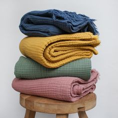 several blankets stacked on top of each other in front of a white wall and wooden stool