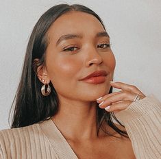 a woman in a tan sweater is posing for the camera with her hand on her chin