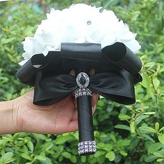 a hand holding a black and white flower bouquet with diamond brooches on it