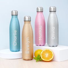 three stainless steel water bottles sitting on top of a white stand next to an orange