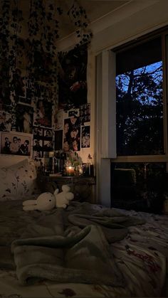 an unmade bed in front of a window with pictures on the wall