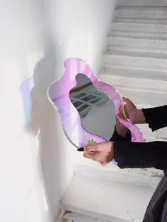 a woman is holding a mirror in her hand while sitting on the steps with white paint