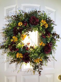 a wreath hanging on the front door with flowers and greenery around it's edges