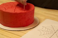 a person is decorating a red cake with spider webs on the icing