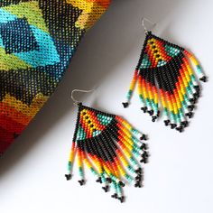 Hand woven by indigenous Embera Chami artisans, these seed bead earrings represent a piece of Colombian culture, fusing modern designs with ancient tribal craftsmanship. The Embera Chami tribe are known for their intricate and colorful bead work and these earrings do not disappoint. Each pair features beautiful bead detailing in a unique FOSTERIE exclusive small batch pattern. Materials: Seed beadsSize: Approximately 3 inches from top of hook, 1.5 inch wide Handmade Modern Multicolor Earrings, Modern Multicolor Dangle Jewelry, Modern Handmade Rainbow Jewelry, Artisan Black Beaded Dangling Earrings, Multicolor Dangle Jewelry With Black Beads, Artisan Black Beaded Drop Earrings, Teardrop Multicolor Jewelry For Festivals, Multicolor Teardrop Jewelry For Crafting, Artisan Multicolor Jewelry With Black Beads