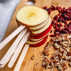 sliced apples, chopped walnuts and cranberries on a cutting board with wooden utensils