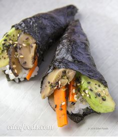 two sushi rolls with carrots, cucumber and sesame seeds on them