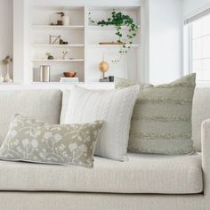 a white couch with pillows on it in front of a book shelf filled with books