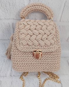 a beige handbag with a gold chain hanging from it's side, against a white brick wall