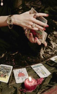 a woman's hands holding tarot cards next to a candle