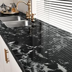 a black marble counter top with gold faucets and brass handles in a kitchen