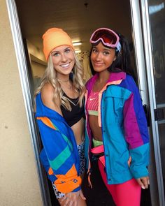 two women standing next to each other in front of an open door wearing ski gear