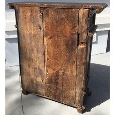 an old wooden cabinet sitting on top of a cement floor next to a building with white siding