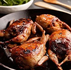 chicken legs in a skillet next to a bowl of greens and wooden utensils