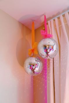 two disco balls hanging from the ceiling in front of pink curtains and drapes with bows on them