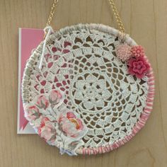 a white doily with pink flowers hanging from a chain on a wooden table next to a card