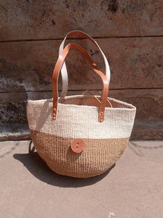 "Natural sisal kiondo bag with stitched leather straps. Ideal for the beach 🏖️, with a casual wear and a perfect accessory for an evening out with friends. This unique tote bag is handmade by a group of ladies in a remote rural village in Machakos, Kenya. DIMENSIONS Bottom width: 10\"/25.5cm Top width: 14\"/35.56cm Depth: 10\"/25.5cm Straps: 15\"/38cm SHIPPING All orders ship via DHL Express (3-5) days delivery time." Basket-shaped Bucket Bag In Woven Leather And Jute, Brown Jute Bucket Bag In Basket Shape, Beige Jute Basket Bucket Bag, Brown Jute Basket Bucket Bag, Brown Jute Basket-shaped Bucket Bag, Jute Bucket Bag For Market, Eco-friendly Basket Bucket Bag With Leather Handles, Eco-friendly Basket-shape Bucket Bag With Leather Handles, Jute Straw Bag With Leather Handles Bucket Shape