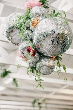 disco balls hanging from the ceiling with flowers and greenery on them in an indoor space