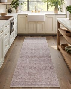 a kitchen with white cabinets and wooden floors, along with a pink rug on the floor