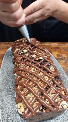 a person cutting into a piece of cake with chocolate icing and nuts on top