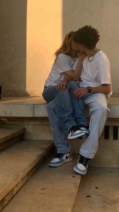 two people are sitting on some steps with their heads to each other and one is kissing the other