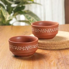 two brown bowls sitting on top of a wooden table next to coasters and a potted plant