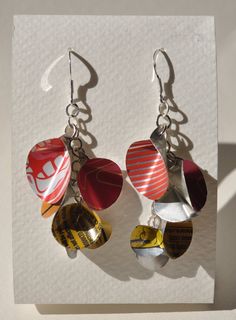 two pairs of earrings hanging from hooks on a piece of white paper with red and yellow designs