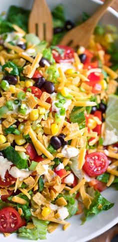 a salad with black olives, tomatoes, corn and lettuce in it