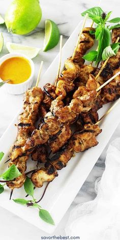 grilled chicken skewers on a white plate with limes and dipping sauce