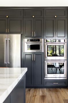 a kitchen with gray cabinets and white counter tops, stainless steel ovens and an island