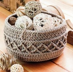 a crocheted basket filled with balls of yarn on top of a wooden floor