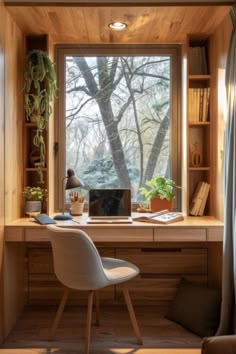 a desk with a laptop computer on top of it next to a window filled with books and plants