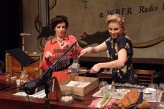 two women are standing at a table with food and microphones in front of them