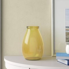 a yellow vase sitting on top of a white table next to a book and cup