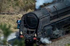 a man in a suit standing next to an old fashioned steam engine train on the tracks