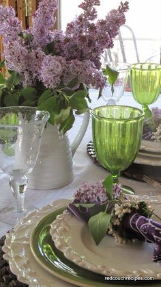 the table is set with purple flowers and green glassware