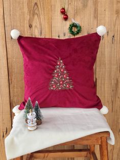 a red christmas pillow sitting on top of a wooden chair next to a small tree