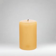 a yellow pillar candle on a white background with a small black dot in the middle